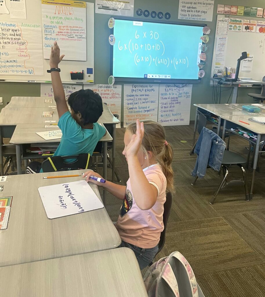 A male and female student both raise their hands to answer a question during Math Club.
